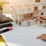 A person is working on some papers with a model of a house.