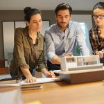Three people looking at a model of a house.