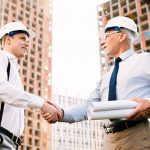 Two men shaking hands in front of a building.