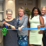 A group of people standing around cutting the ribbon.