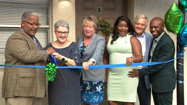 A group of people standing around cutting the ribbon.